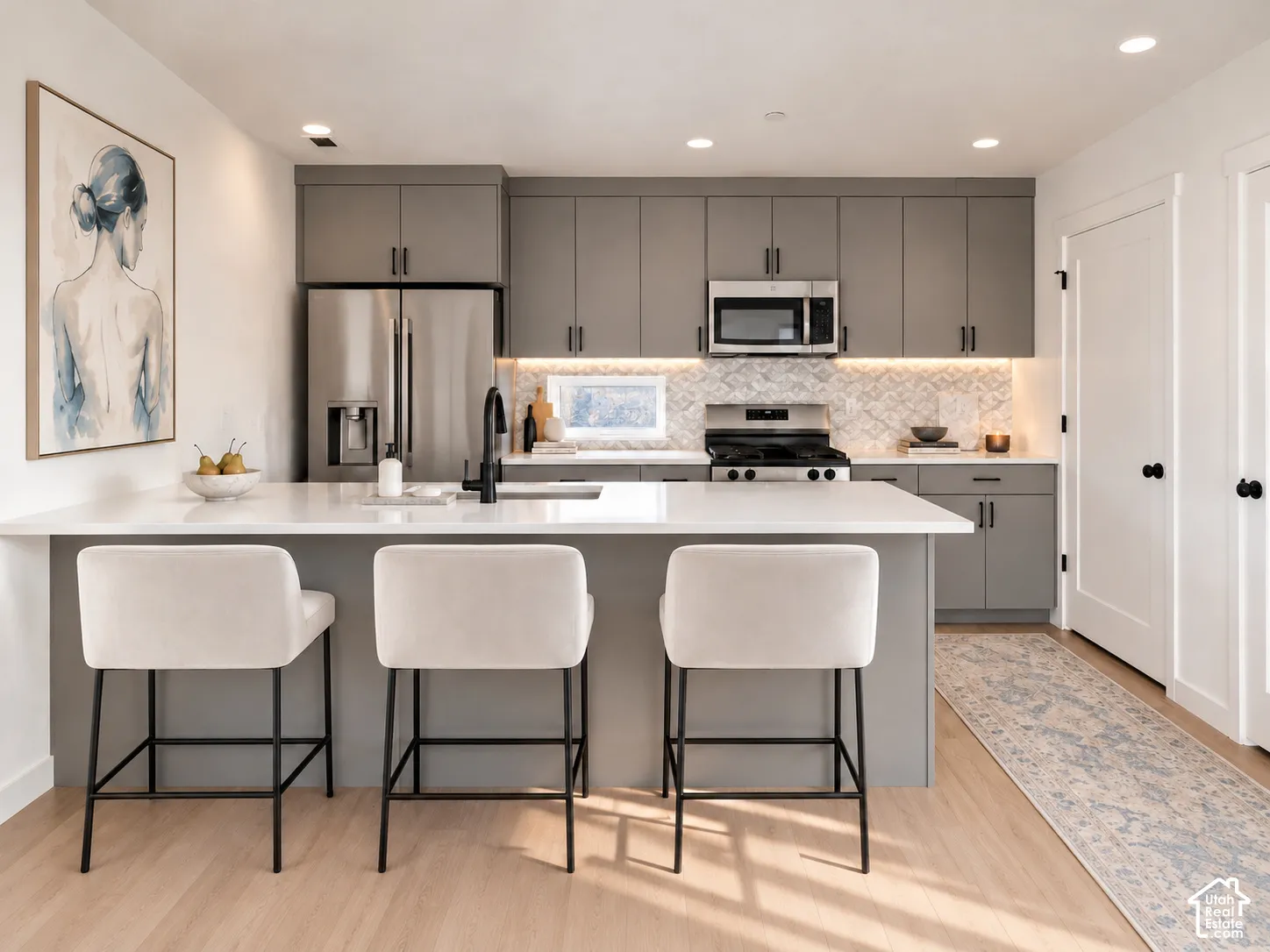 Kitchen featuring grey flat-panel cabinetry, a central island with white countertop, stainless steel appliances, patterned tile backsplash, and wood-finish flooring