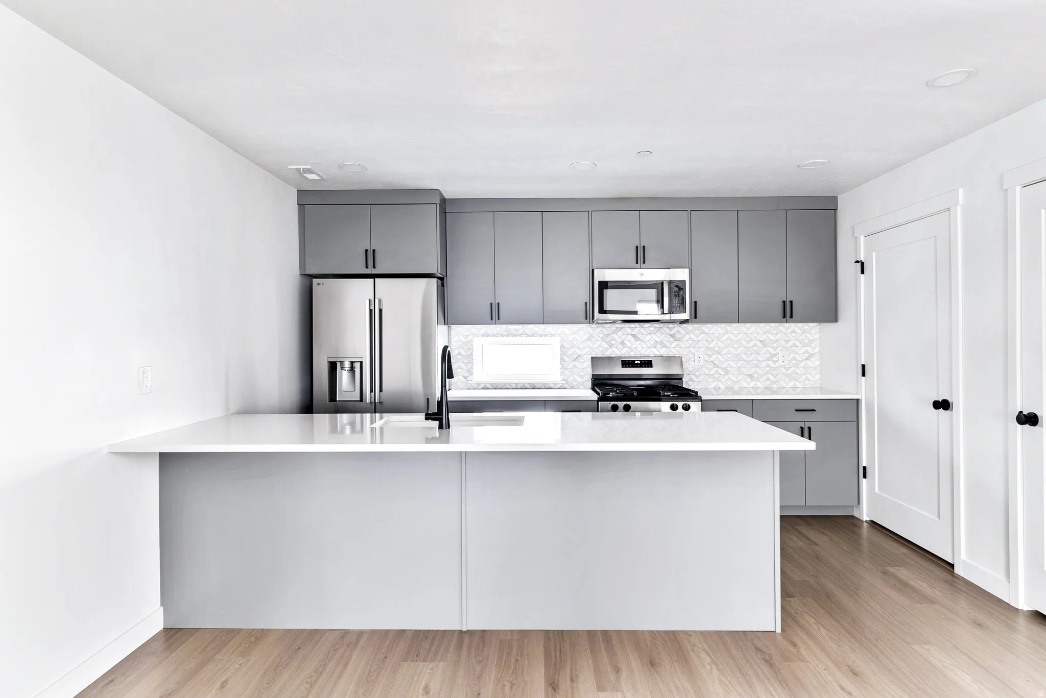 Kitchen featuring a central island with a sink, stainless steel appliances, grey cabinetry, and a patterned backsplash