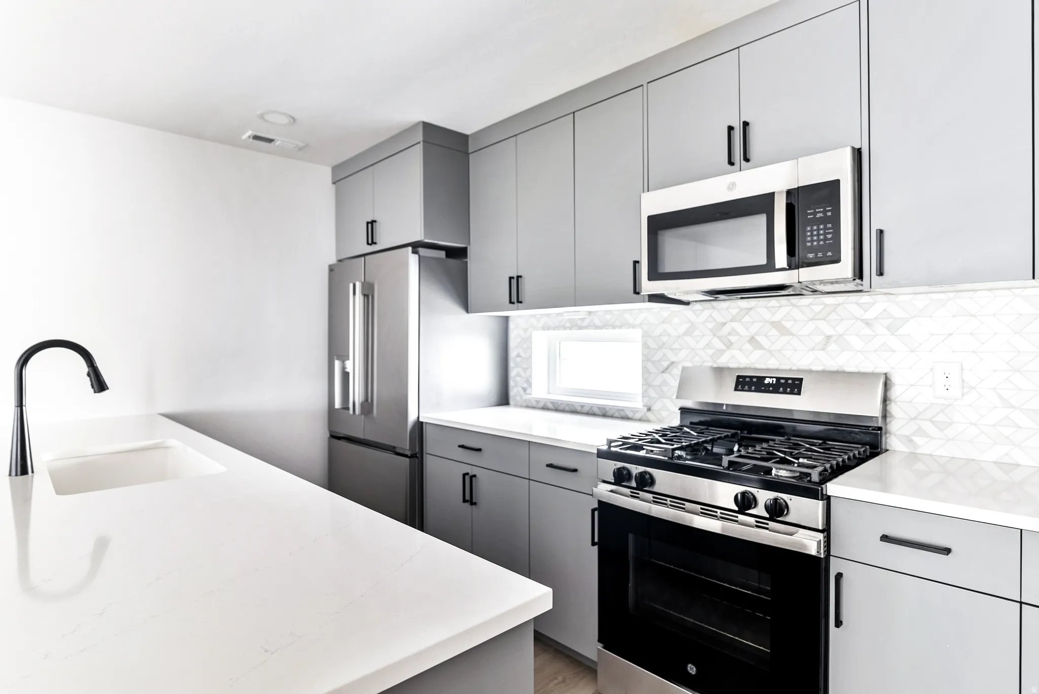Modern kitchen featuring gray flat-panel cabinetry, stainless steel appliances, white countertops, and a mosaic tile backsplash