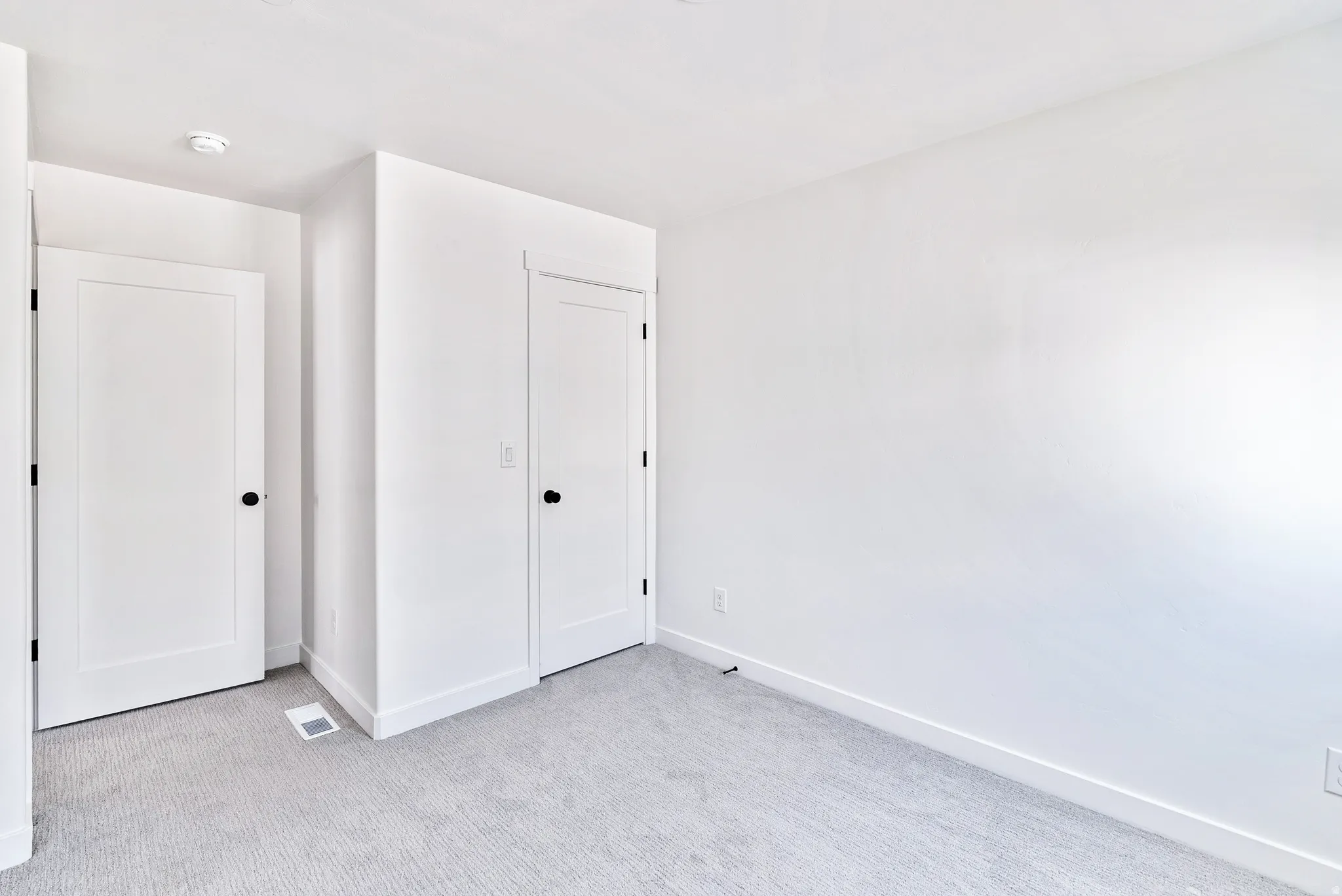 Light gray carpeting, white walls, and white interior doors with matte black hardware