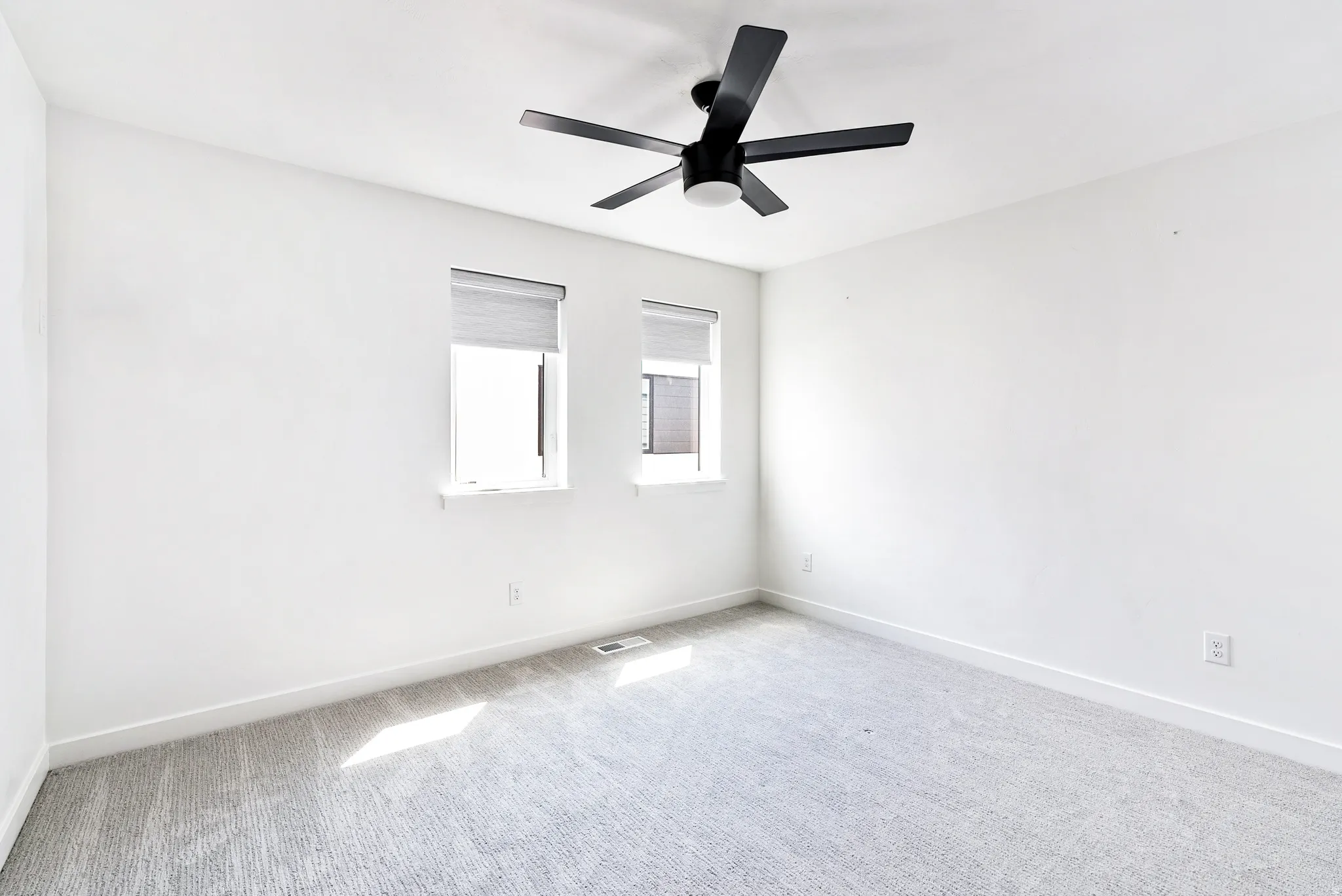 White walls with a black ceiling fan, two windows, and light gray carpet