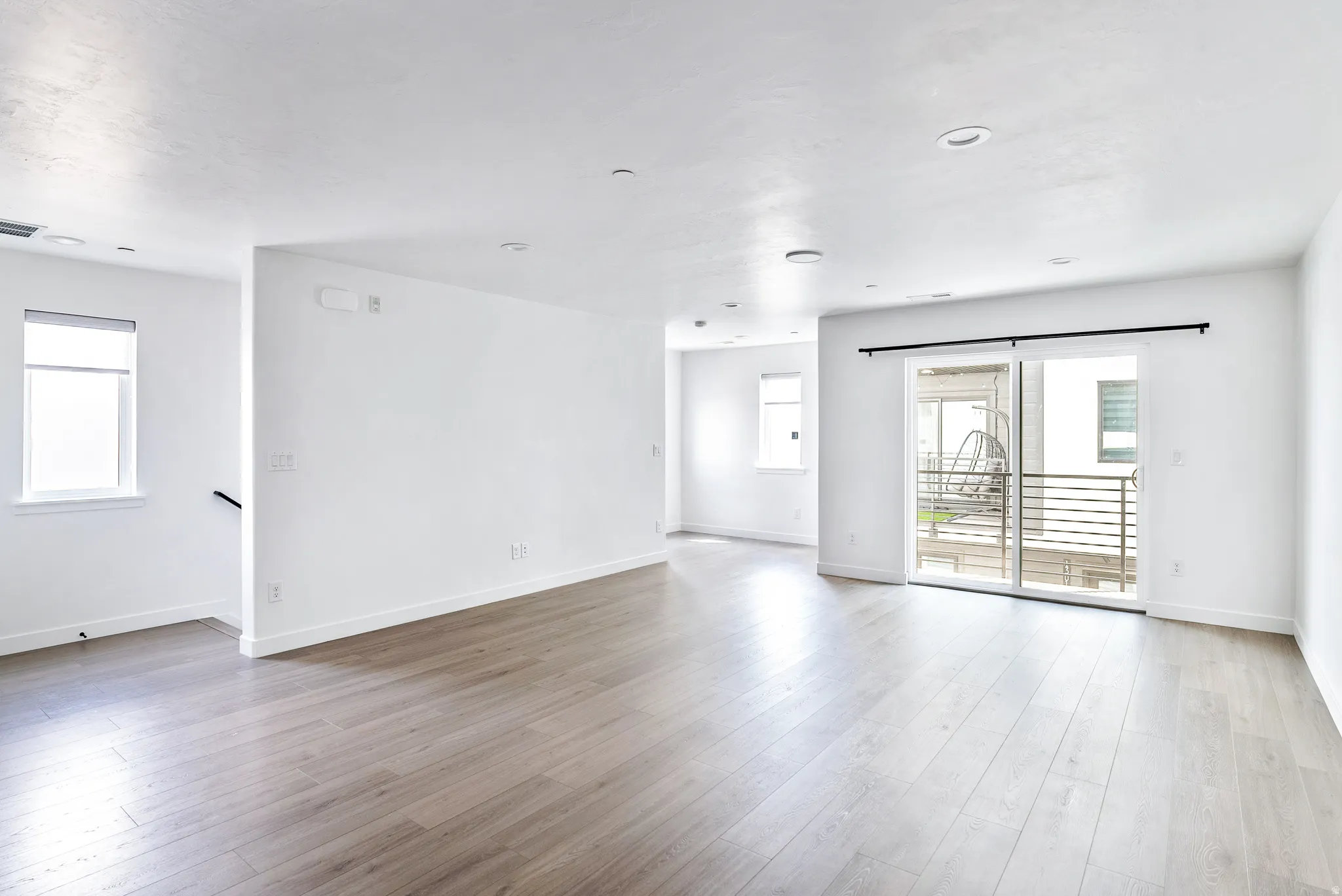 Recessed lighting, wood-finish flooring, white walls, multiple windows, and a sliding glass door to an exterior balcony