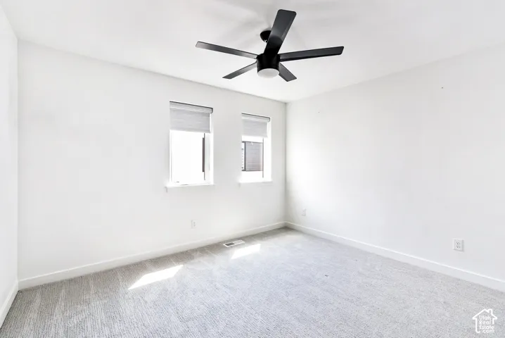 Room featuring a ceiling fan, two windows, and light-colored carpeting