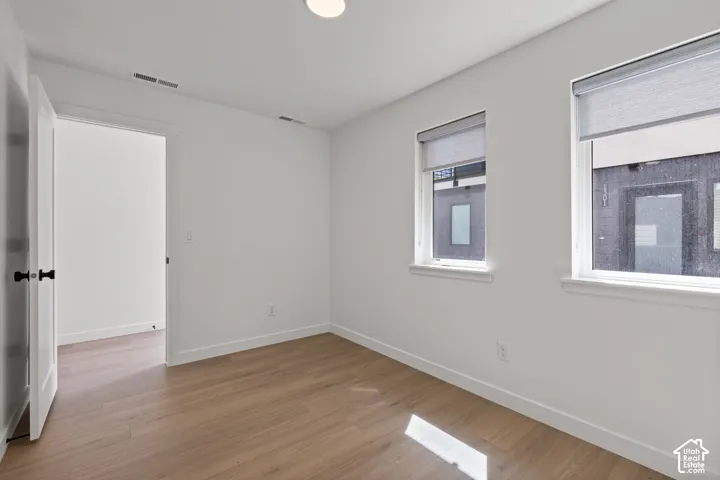 Wood-finish flooring, white walls, two windows with roller shades, recessed lighting, and a white door with black hardware