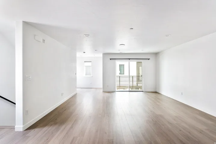 Wood-finish flooring, white walls, recessed lighting, and a sliding glass door with a balcony