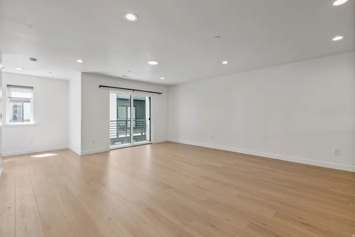 Bright living space featuring light wood-finish flooring, recessed lighting, and a sliding glass door to a balcony with metal railings
