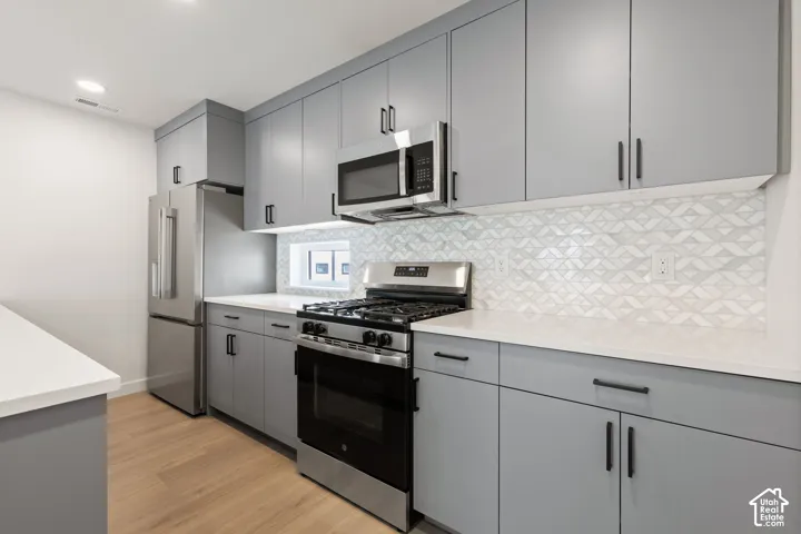Modern kitchen featuring light gray cabinetry, stainless steel appliances, white countertops, and wood-finish flooring