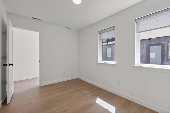 Wood-finish flooring, white walls, two windows with roller shades, recessed lighting, and a white door with black hardware