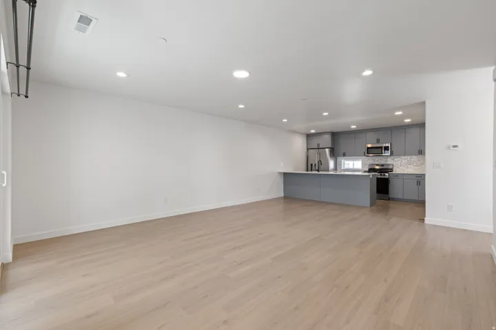 Open-concept living space featuring wood-finish flooring, recessed lighting, and a kitchen with gray cabinetry, a white countertop, and stainless steel appliances