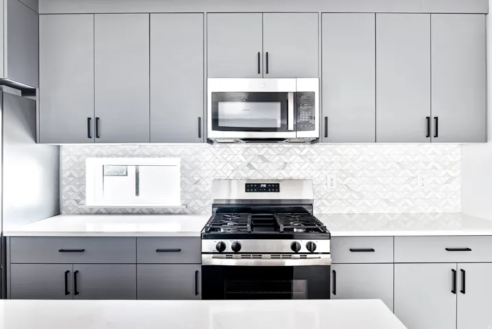 Light grey cabinetry with black hardware, stainless steel range with oven, built-in stainless steel microwave, white countertops, and geometric pattern tile backsplash