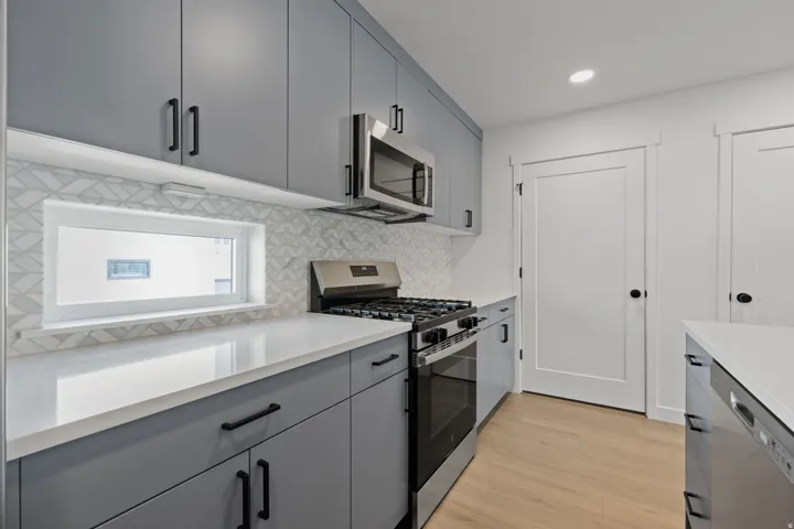 Sleek kitchen featuring light gray cabinetry, white countertops, stainless steel appliances, and wood-finish flooring