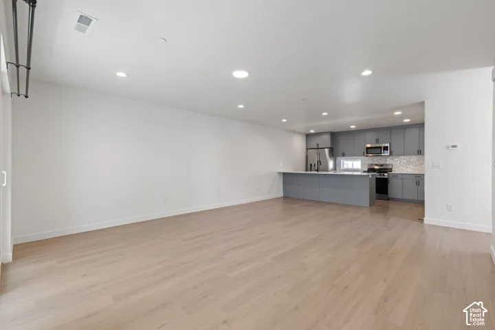 Open-concept living space featuring wood-finish flooring, recessed lighting, and a kitchen with gray cabinetry, a white countertop, and stainless steel appliances