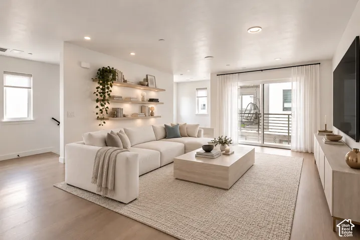 Living area featuring light-toned wood-finish flooring, recessed lighting, and wall-mounted floating shelves with integrated accent lighting