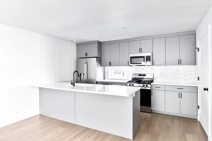 Kitchen featuring wood-finish flooring, white countertops, gray cabinetry, stainless steel appliances, and a tiled backsplash
