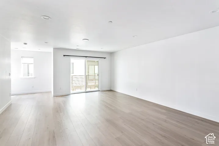 Spacious room with light wood-finish flooring, recessed lighting, and a sliding glass door