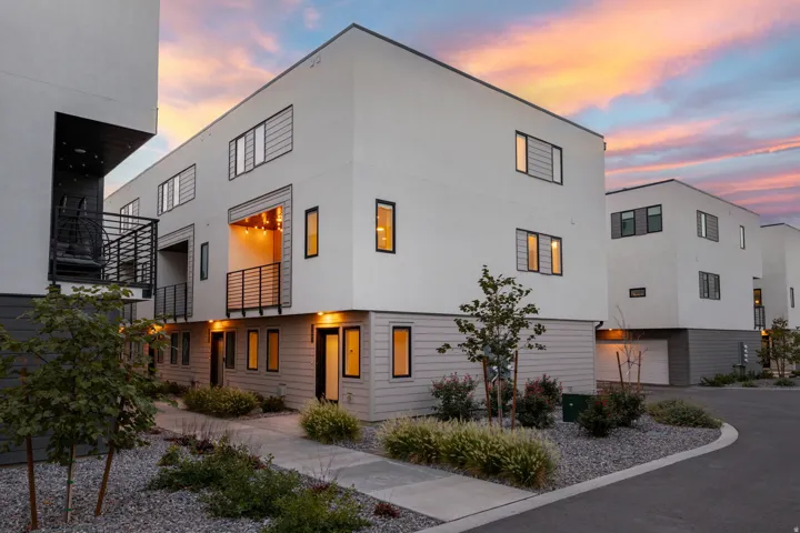 Modern architectural exterior featuring white stucco, dark gray siding, multiple balconies with black railings, and integrated garage access