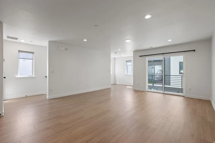 Expansive open-concept room featuring wood-finish flooring, white walls, recessed lighting, and a sliding glass door to an outdoor space with horizontal railings