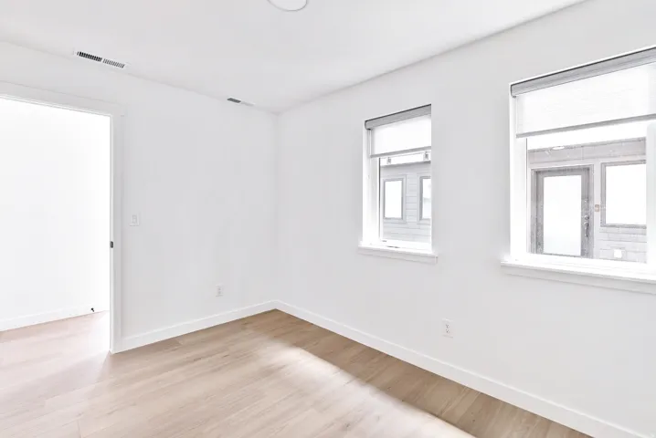 Bright room featuring wood-finish flooring, two large windows with roller shades, and an open doorway
