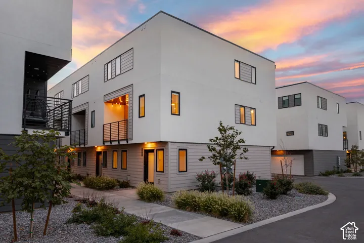 Modern architectural exterior featuring white stucco, dark gray siding, multiple balconies with black railings, and integrated garage access