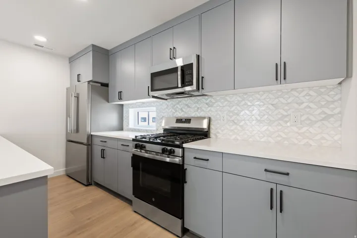 Modern kitchen featuring light gray cabinetry, stainless steel appliances, white countertops, and wood-finish flooring