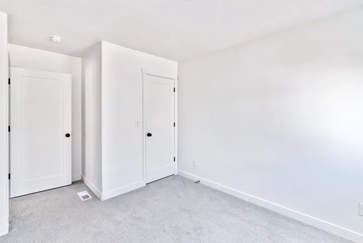 Clean white walls, light-toned carpet, and two paneled doors with black hardware