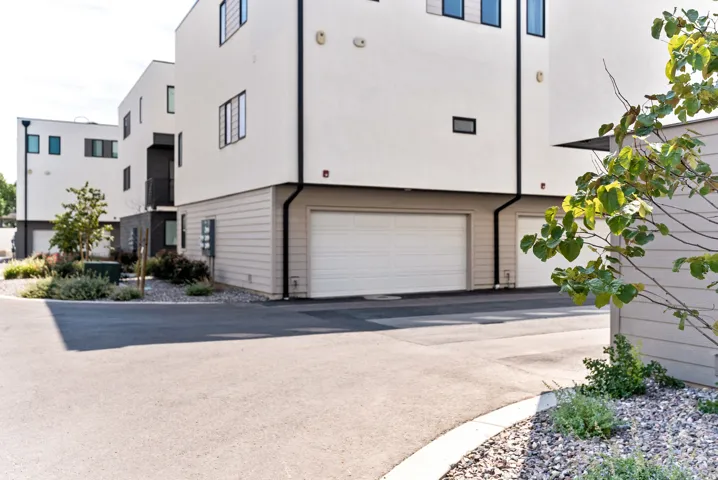 White stucco exterior with black trim, integrated garage, and landscaped beds