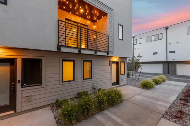 Modern exterior with a private balcony featuring a black metal railing, a ground-level patio, and contemporary landscaping