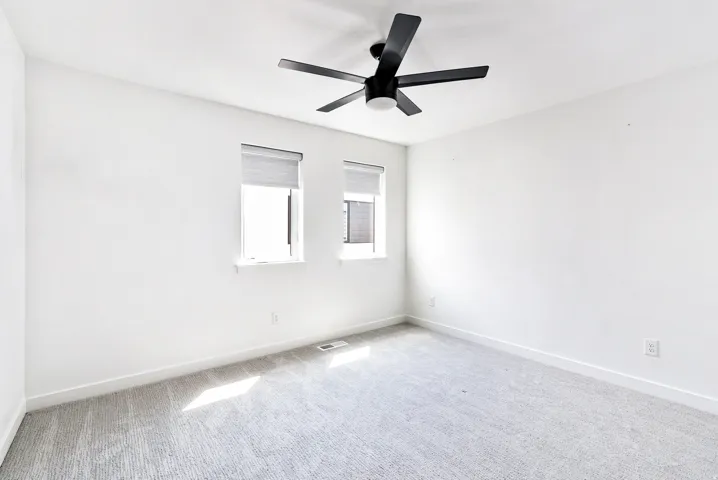 Room featuring a ceiling fan, two windows, and light-colored carpeting