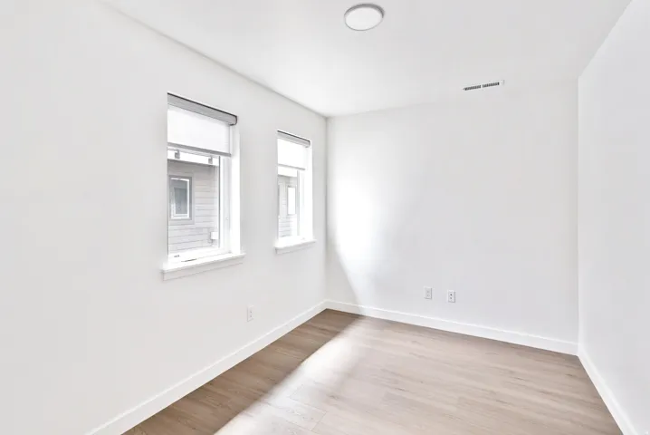 Bright room with two windows, wood-finish flooring, and white walls