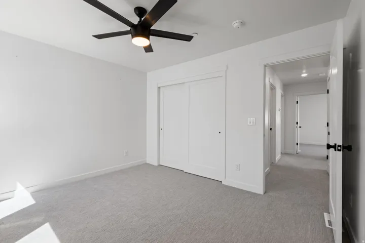 Recessed lighting, light gray carpet, white walls, black ceiling fan, and white sliding closet doors
