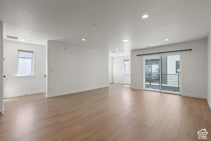 Expansive open-concept room featuring wood-finish flooring, white walls, recessed lighting, and a sliding glass door to an outdoor space with horizontal railings
