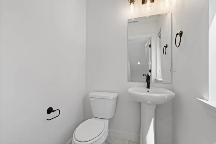 Pedestal sink with black-finish faucet, rectangular mirror, and three-light vanity fixture