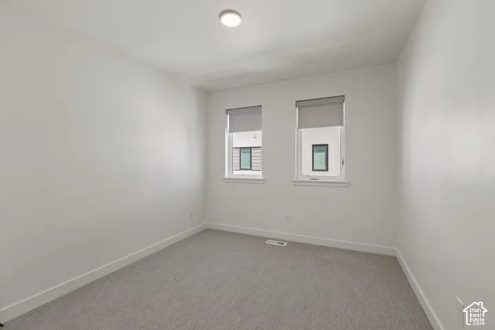 Recessed ceiling light, two windows with roller shades, light grey carpeting, and white baseboards