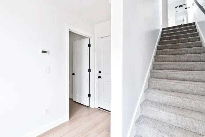 Light wood-finish flooring, white walls, and a gray carpeted staircase