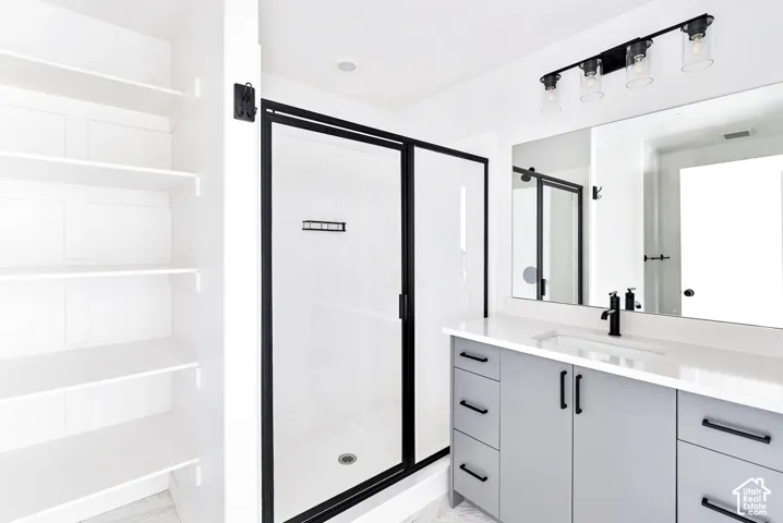 Built-in shelving, matte black framed glass shower, light gray vanity with black hardware, white rectangular undermount sink, and a four-light vanity fixture