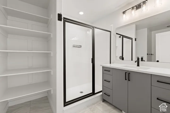 Built-in shelving, glass-enclosed shower with black trim, vanity with integrated sink and white countertop, black fixtures, and tile flooring