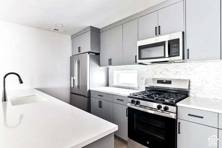 Sleek kitchen featuring gray cabinetry, stainless steel appliances, a built-in microwave, white countertops, and a tile backsplash