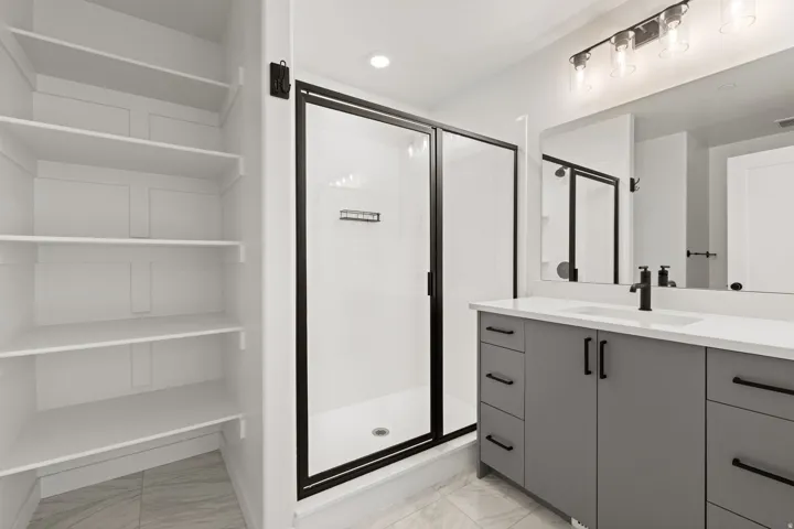 Built-in shelving, glass-enclosed shower with black trim, vanity with integrated sink and white countertop, black fixtures, and tile flooring