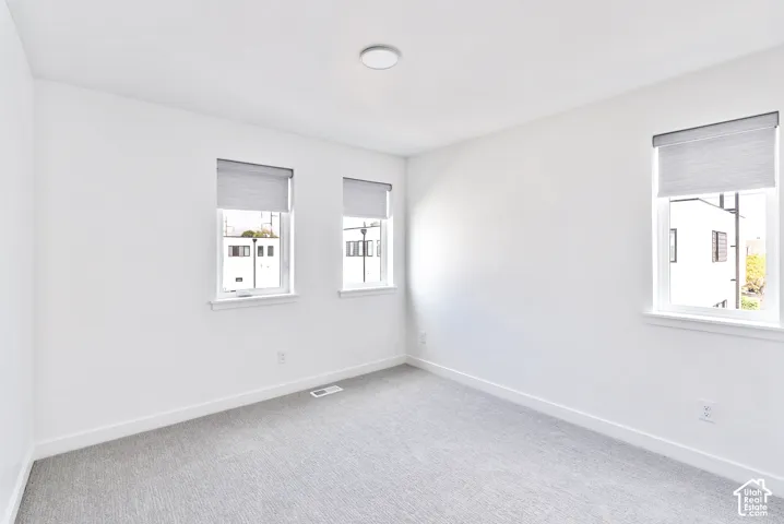 Recessed ceiling light, multiple windows with roller shades, light-toned carpeting, and white walls