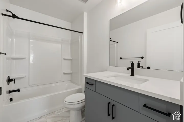 Bathroom featuring a white tub and shower surround, a vanity with grey cabinetry, a white countertop, and a rectangular sink