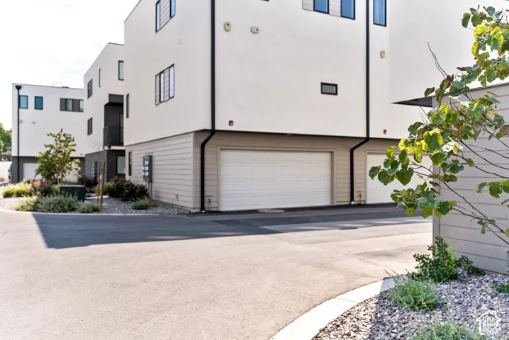 White stucco exterior with black trim, integrated garage, and landscaped beds