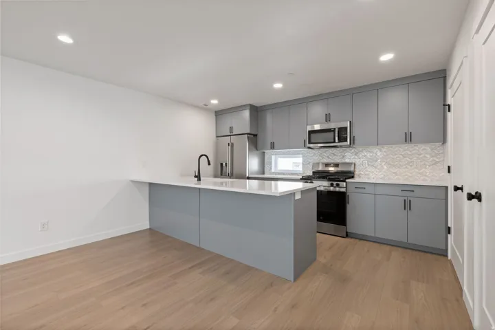 Kitchen featuring gray cabinetry, stainless steel appliances, a white countertop island, a geometric tile backsplash, and wood-finish flooring