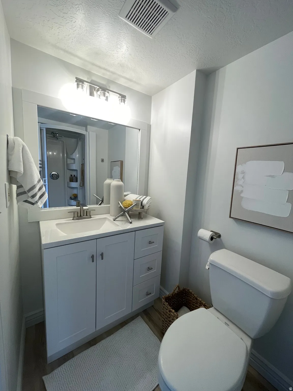 White vanity with a built-in sink, stainless steel faucet, and overhead bar lighting