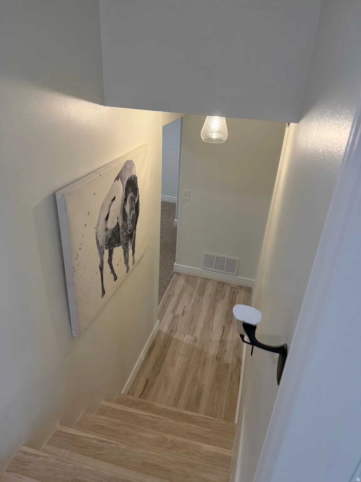 Wood-finish stairs and flooring with a black metal handrail and clear glass pendant light