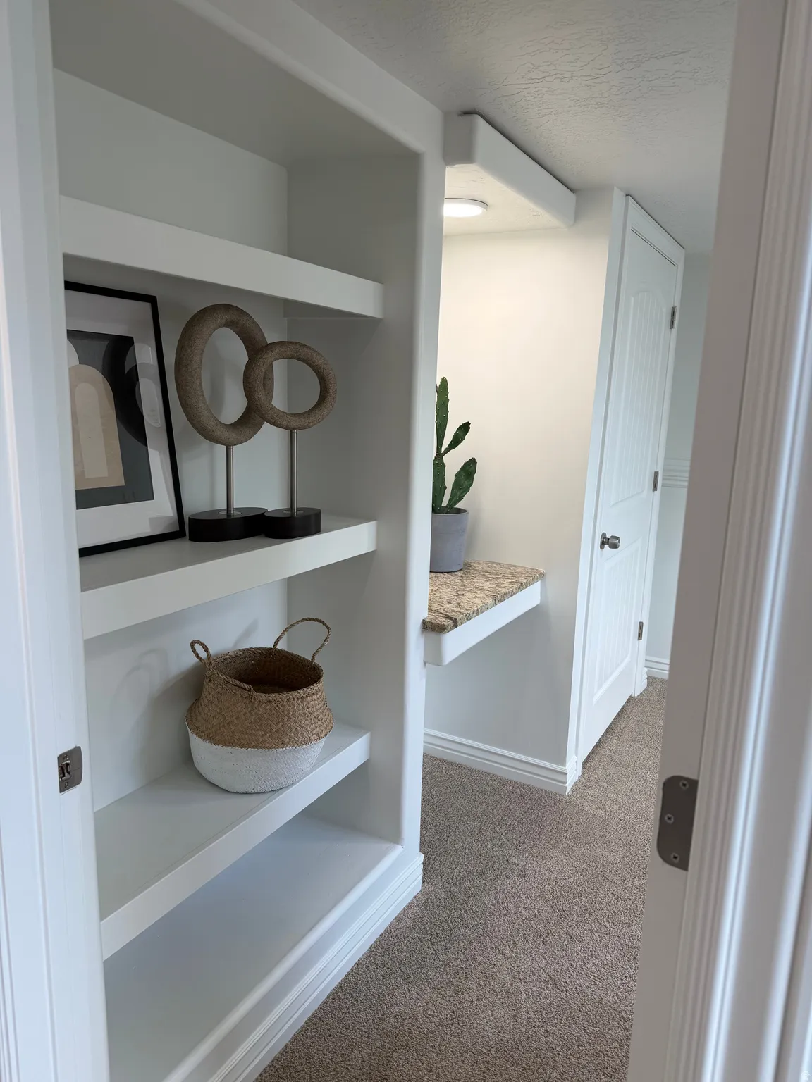 4th bedroom built-in shelving, recessed ceiling light, wall-mounted desk with a stone-finish countertop, white paneled door, and neutral-tone carpeting