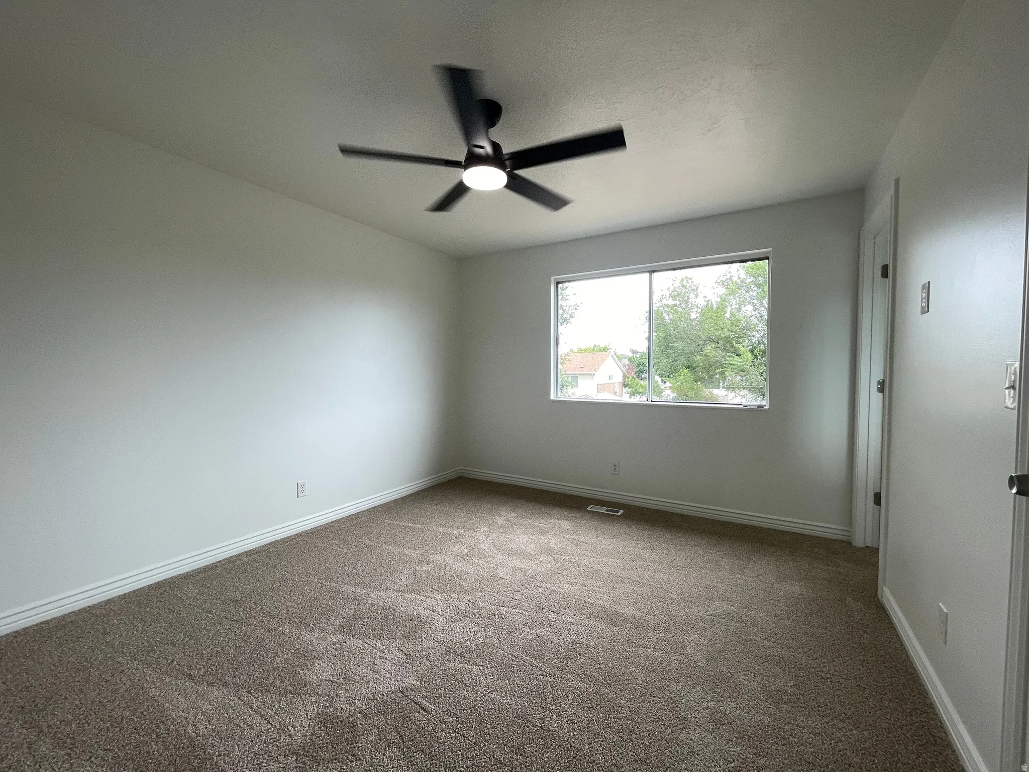 Neutral wall tones, carpeted flooring, a window, a ceiling fan, and a solid-core door
