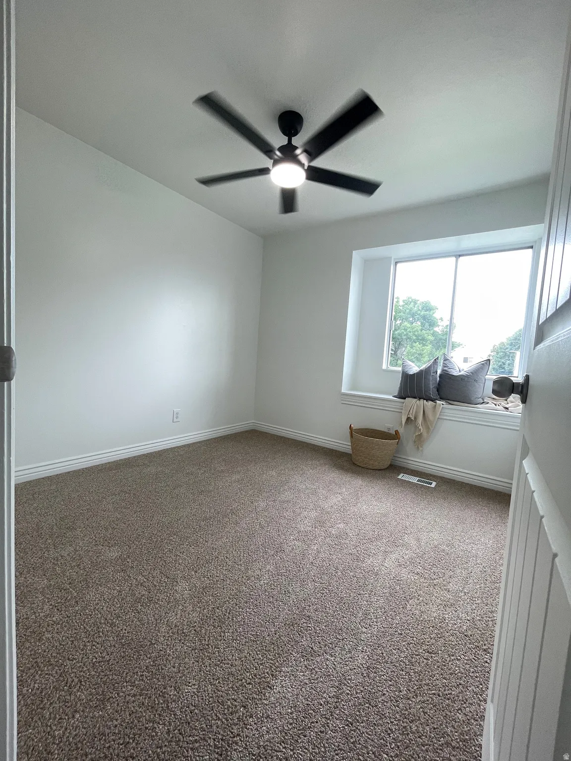 Broadloom carpeting, white painted walls, window with trim, and a ceiling fan with integrated lighting