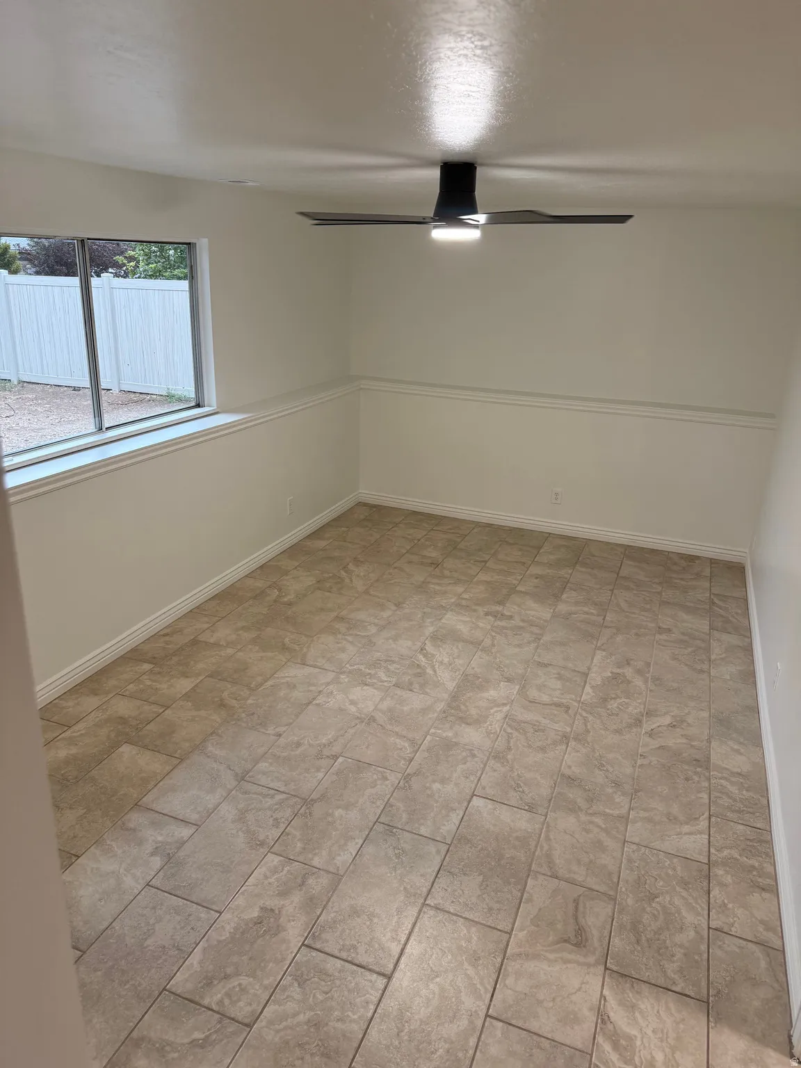 Tile flooring, crisp white walls, modern ceiling fan with integrated lighting, and a large window
