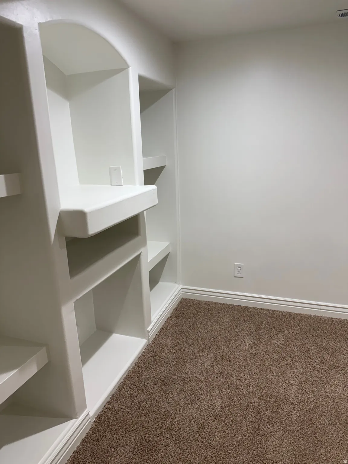 Built-in shelving with arched and rectangular compartments, white painted finish, and brown carpet flooring