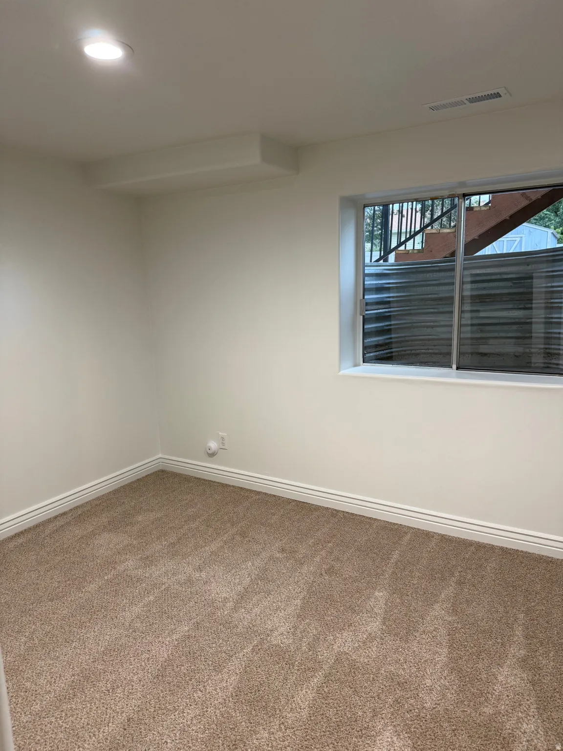 Recessed ceiling lighting, a window with exterior visibility, light-toned carpeting, white walls, and white trim